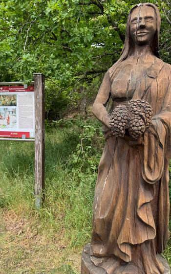Wooden statue of the goddess, Pomona next to a sign on the trail.